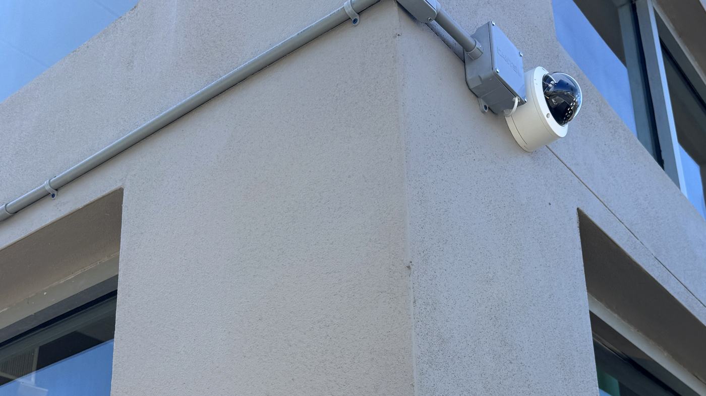 Dome security camera on a commercial building corner with a junction box and conduit run, installed by Allied Technologies